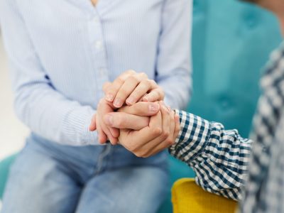 Close up of two people holding hands in  therapy session or support group, copy space